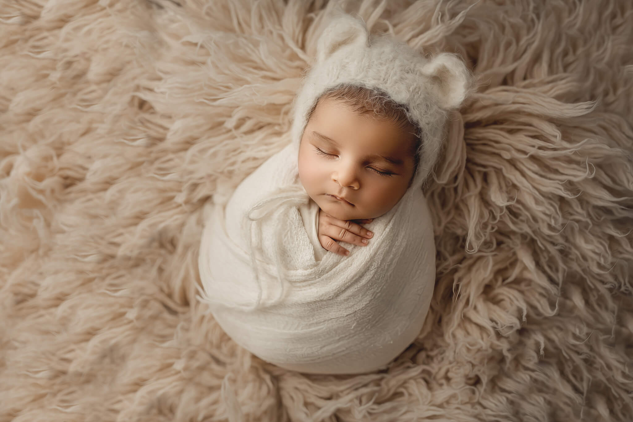 baby wrapped in white wearing cute bear bonnet during newborn shoot