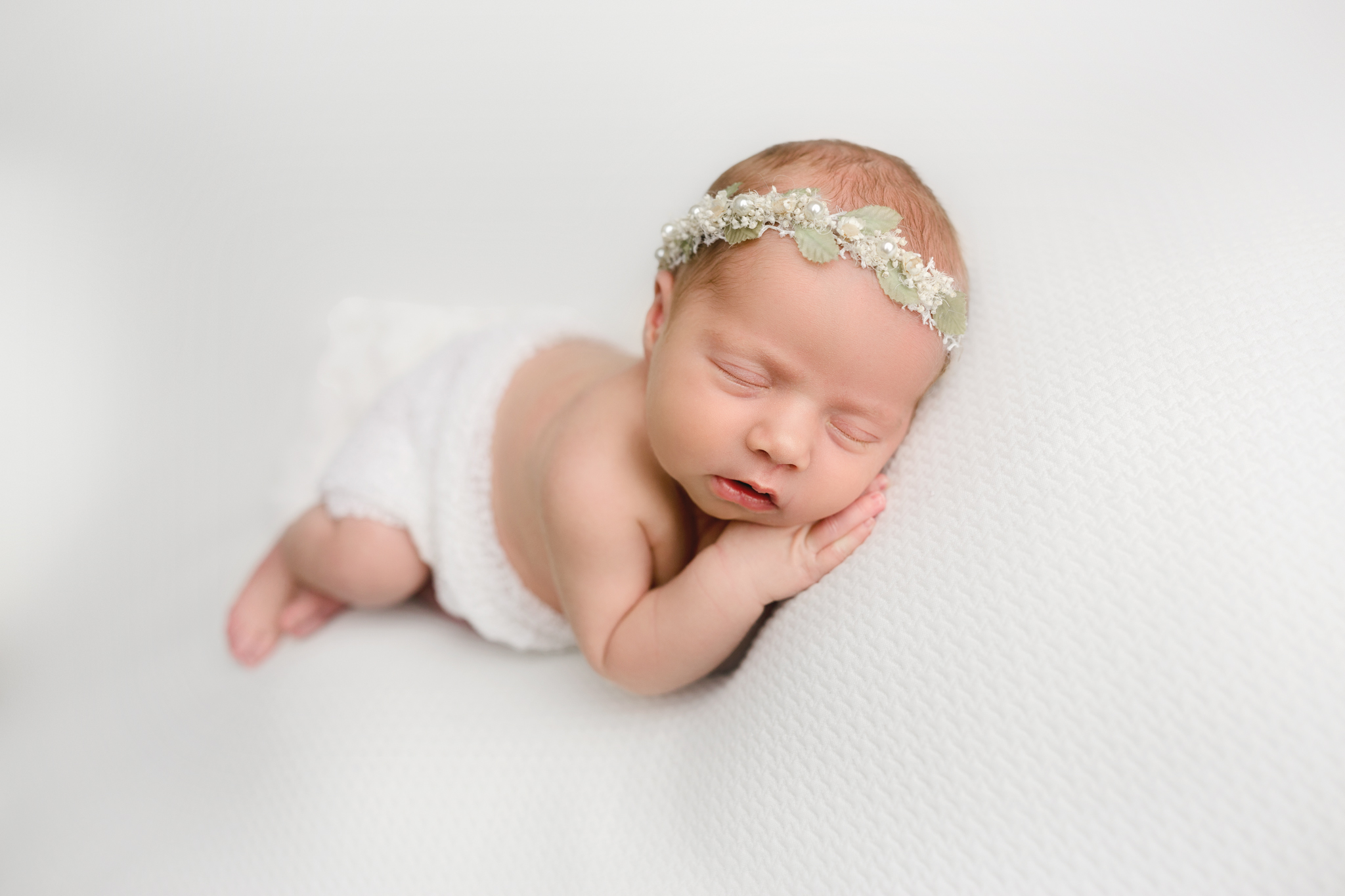 baby girl laying on her side on white backdrop for posed newborn photoshoot in hamilton