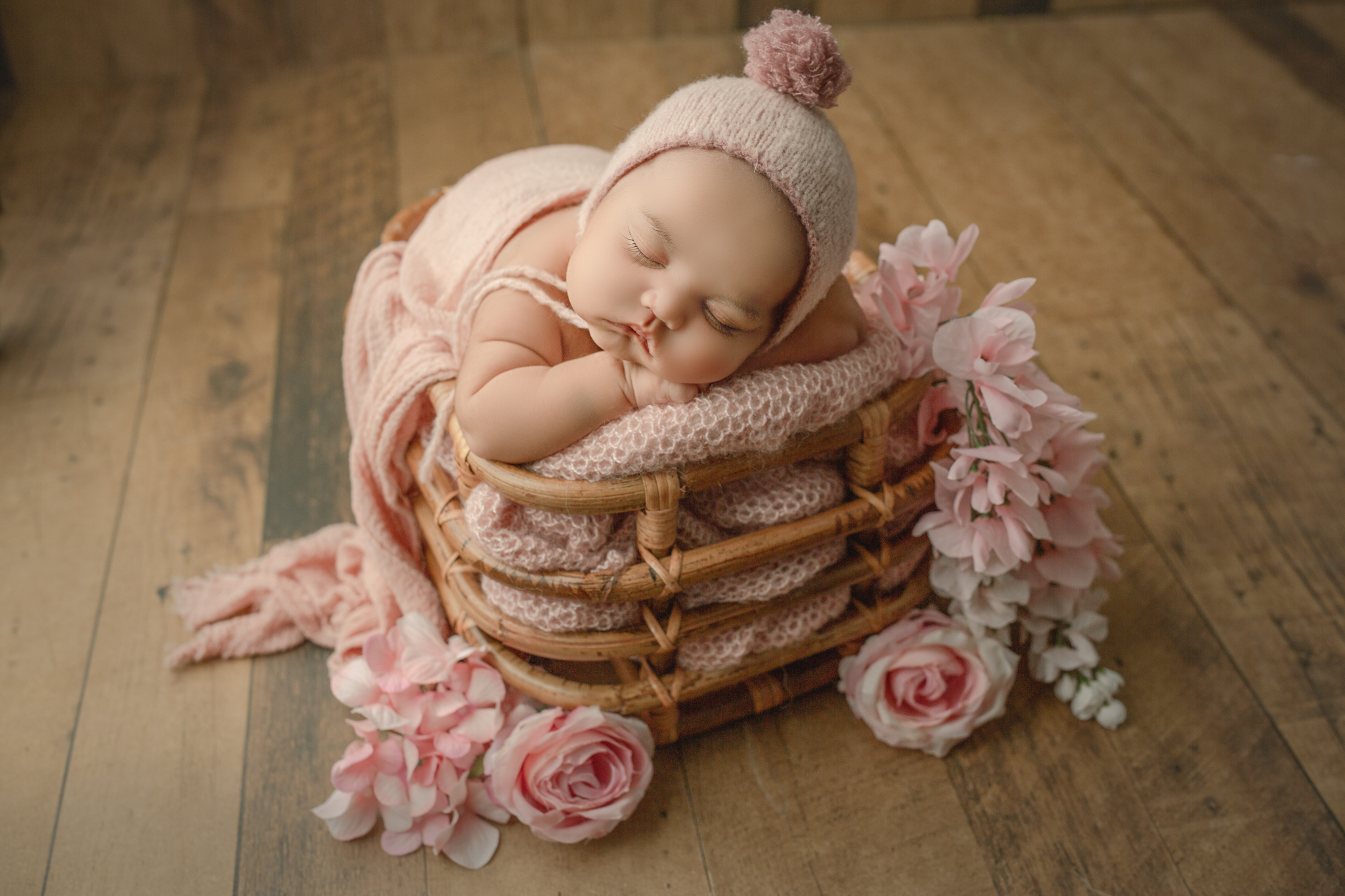 burlington newborn photographer poses baby in bamboo basket with pink florals and pom pom bonnet