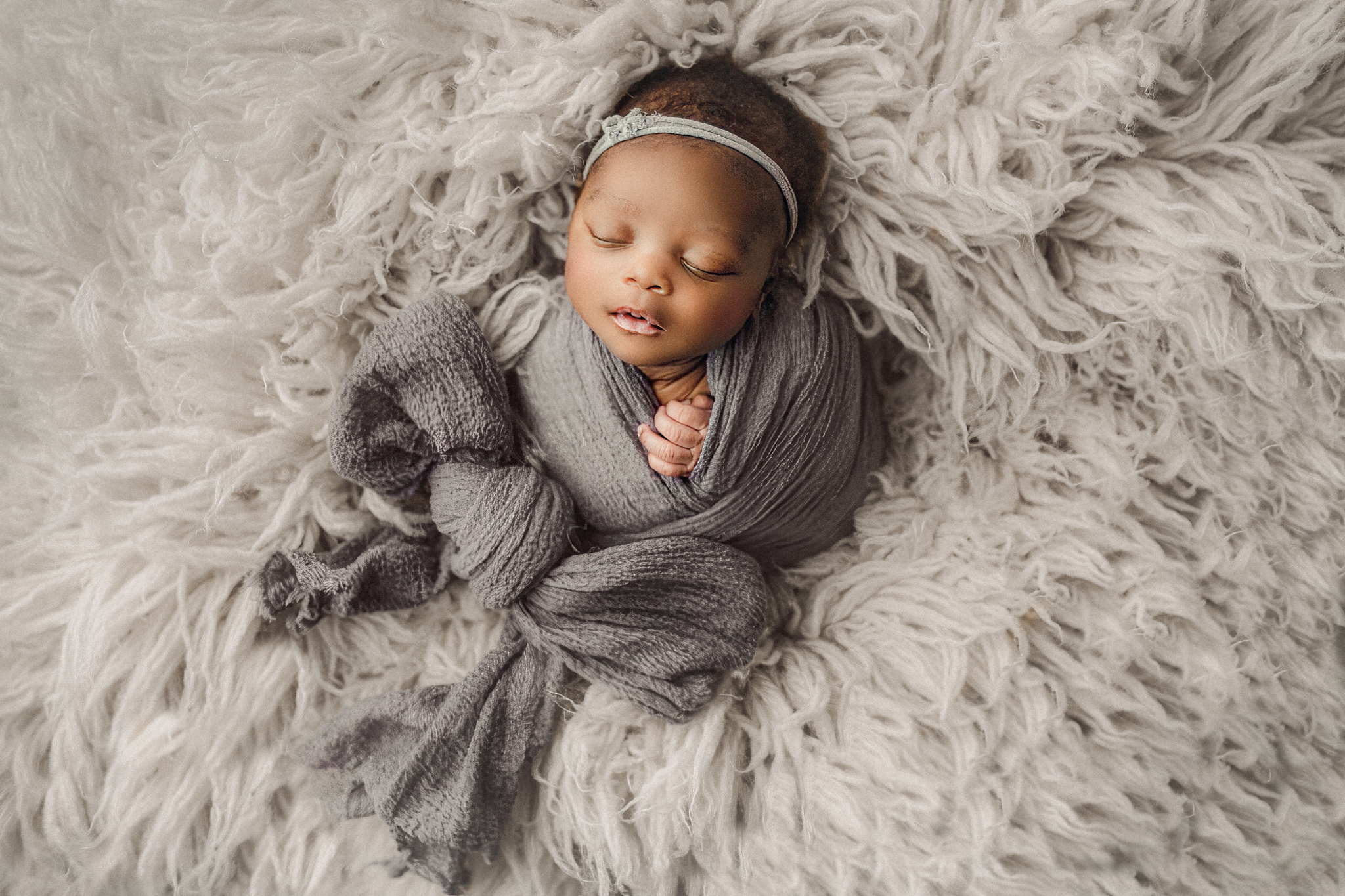 newborn baby wrapped in grey on fluffy rug in hamilton photography studio